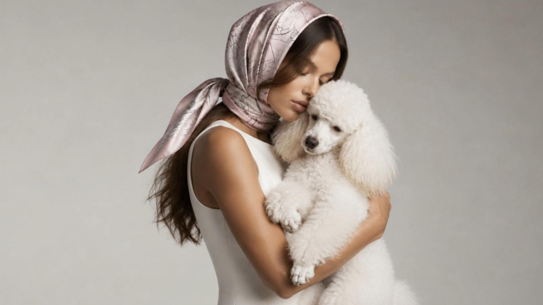 A woman holding a white poodle, wearing a pale scarf, with the words Unmistakably Yours